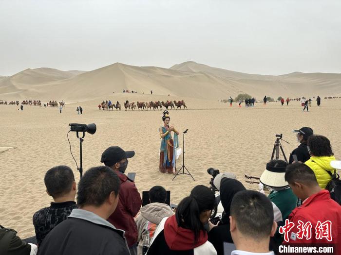 圖為2023年4月底，敦煌大漠“逐舞者”奧楠在鳴沙山月牙泉景區(qū)視頻直播，吸引游人圍觀?！●T志軍 攝
